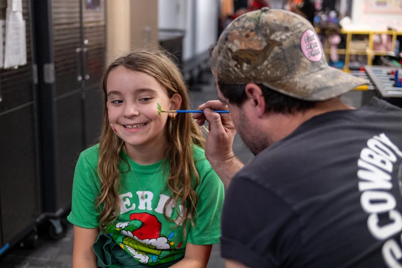 A smiling girl getting her face painted at an FTK holiday party